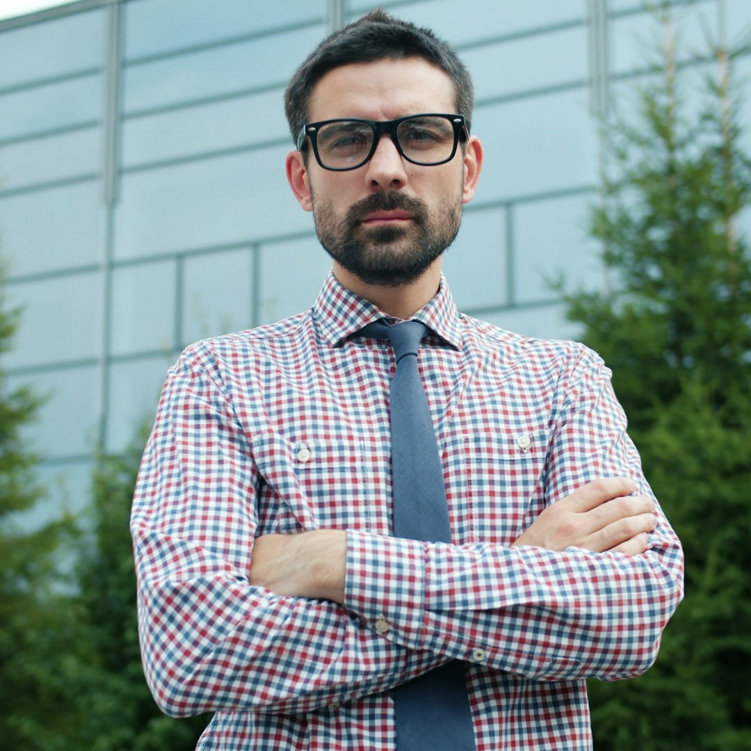 Un homme barbu à lunettes, bras croisés. Illustration du META SHORT intitulé « L'arnaque du coaching de masse », du podcast Méta de Choc.